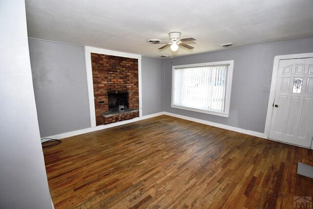 unfurnished living room with ceiling fan, visible vents, baseboards, a brick fireplace, and dark wood finished floors