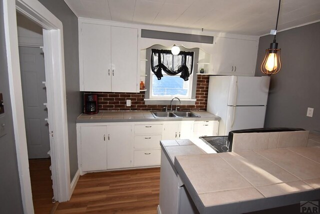 kitchen with tile counters, freestanding refrigerator, white cabinets, and a sink