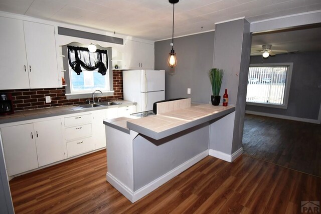 kitchen with a peninsula, a sink, white cabinetry, freestanding refrigerator, and decorative light fixtures