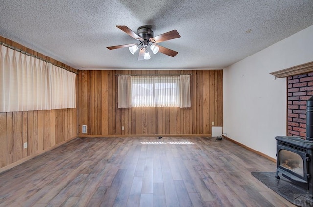 2621 Begonia St, Pueblo, CO 81005 - unfurnished living room with baseboards, a wood stove, a ceiling fan, wooden walls, and wood finished floors
