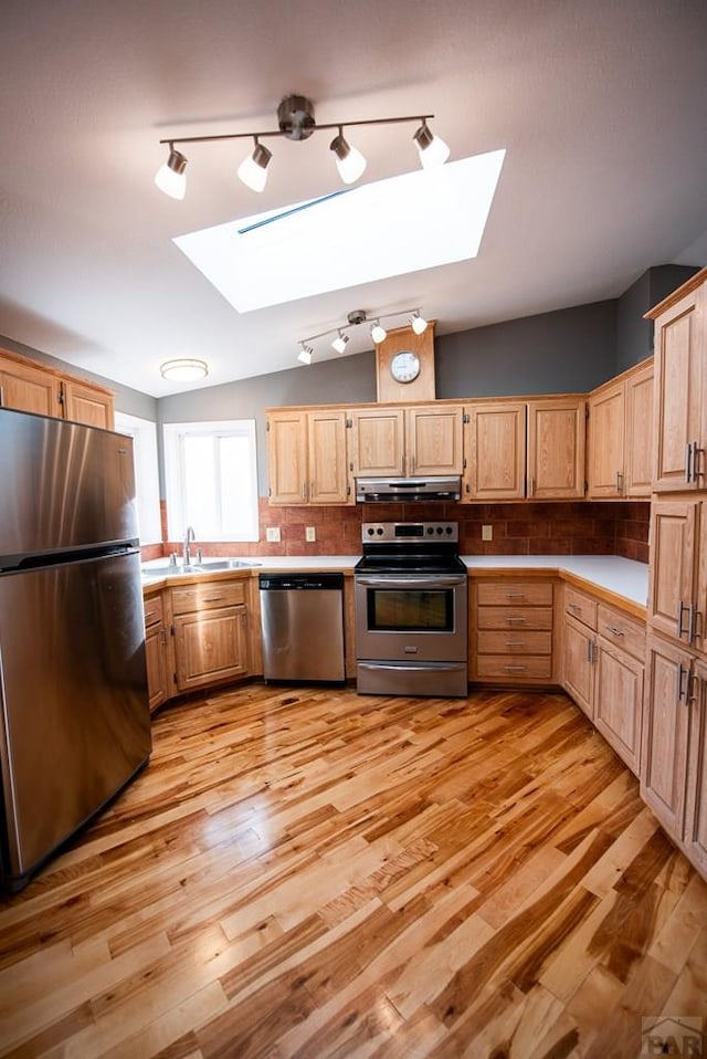 kitchen featuring lofted ceiling with skylight, stainless steel appliances, light countertops, under cabinet range hood, and backsplash