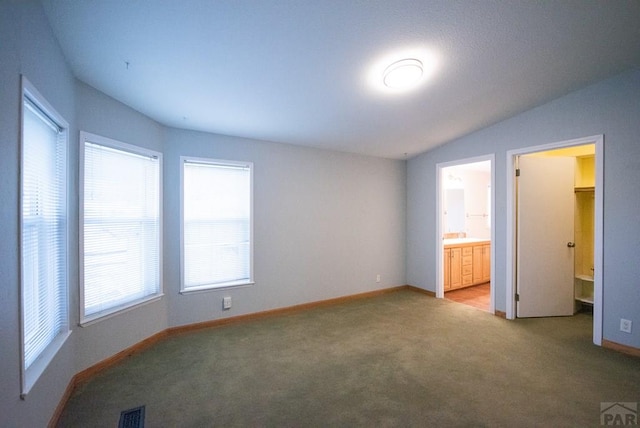 unfurnished bedroom featuring lofted ceiling, visible vents, ensuite bathroom, light carpet, and baseboards