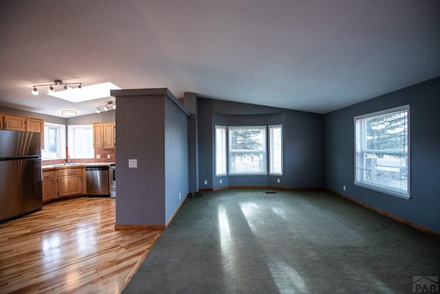 unfurnished living room with plenty of natural light, vaulted ceiling with skylight, and baseboards