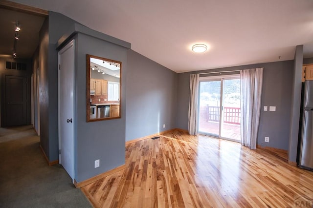 unfurnished room featuring light wood-type flooring, visible vents, vaulted ceiling, and baseboards