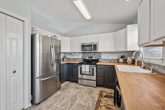 kitchen with lofted ceiling, a sink, stainless steel appliances, white cabinets, and wood counters