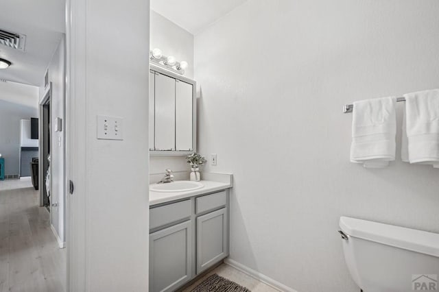 bathroom with visible vents, toilet, wood finished floors, baseboards, and vanity