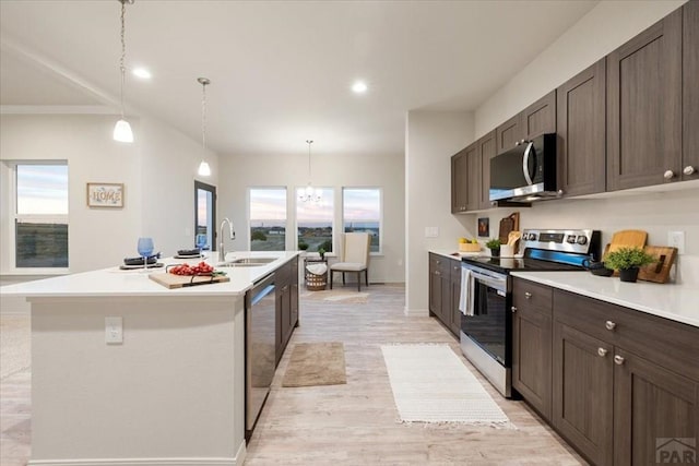 kitchen featuring decorative light fixtures, stainless steel appliances, a sink, light countertops, and a center island with sink