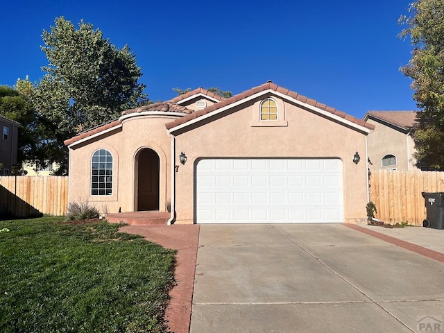 mediterranean / spanish-style house with a tile roof, stucco siding, concrete driveway, fence, and a garage