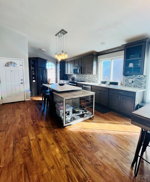 kitchen featuring a kitchen island, glass insert cabinets, appliances with stainless steel finishes, decorative light fixtures, and light countertops