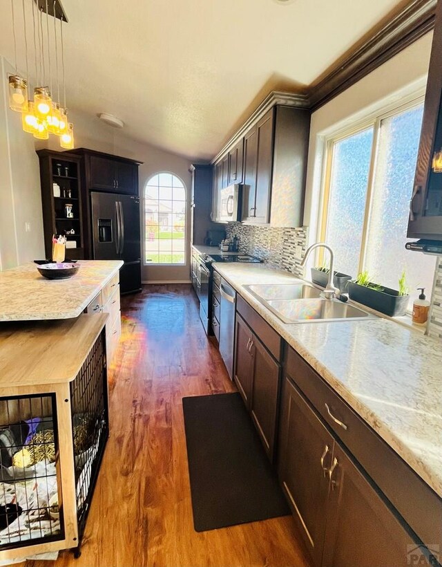 kitchen with decorative backsplash, dark wood finished floors, appliances with stainless steel finishes, hanging light fixtures, and a sink