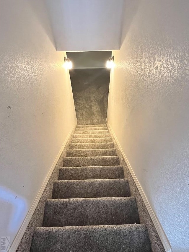 stairs with carpet flooring, a textured wall, and baseboards