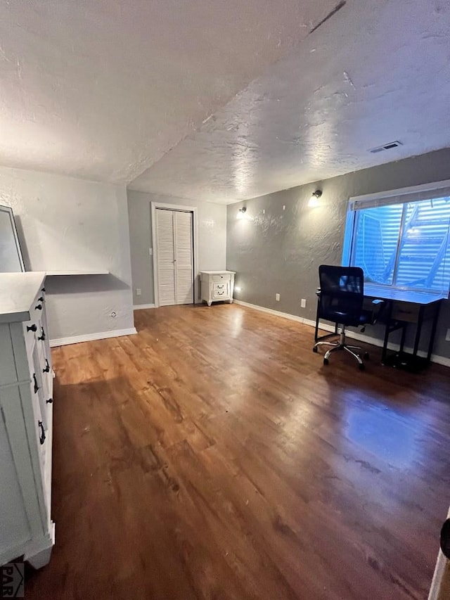 interior space with a textured wall, dark wood-style flooring, visible vents, and baseboards