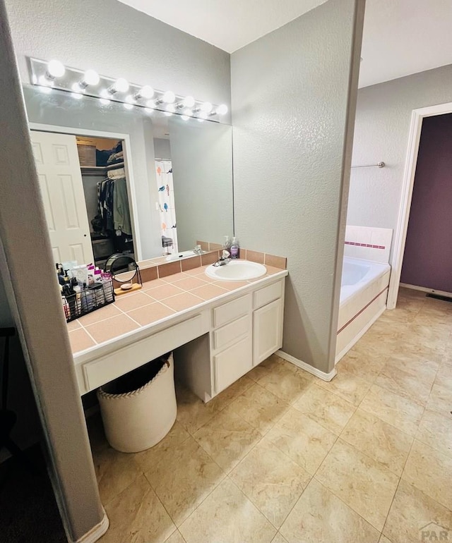 bathroom featuring a textured wall, a garden tub, vanity, baseboards, and a spacious closet