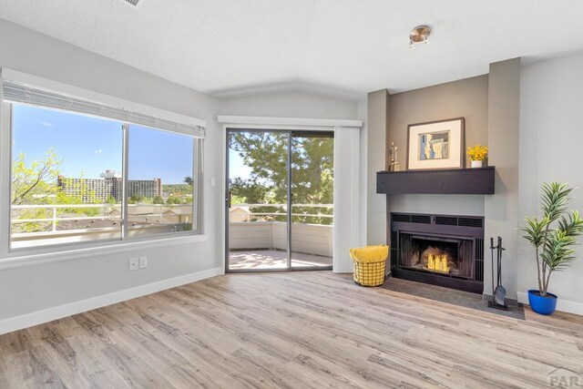 3666 Iguana Dr, Colorado Springs, CO 80910 - unfurnished living room featuring wood finished floors, a fireplace with flush hearth, vaulted ceiling, and baseboards