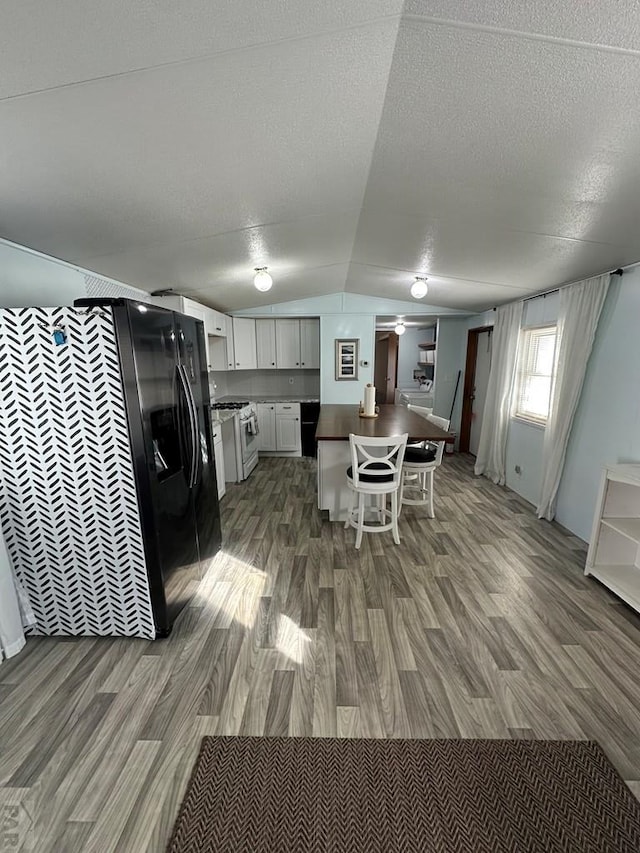 kitchen with a breakfast bar, black fridge, wood finished floors, white cabinetry, and lofted ceiling