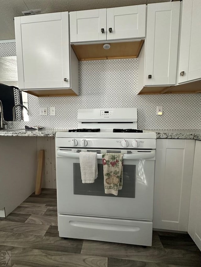 kitchen featuring under cabinet range hood, white range with gas stovetop, decorative backsplash, white cabinetry, and dark wood-style flooring