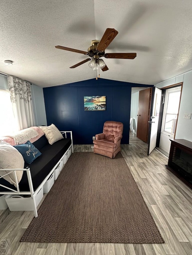 living area with a textured ceiling, wood finished floors, a ceiling fan, and vaulted ceiling