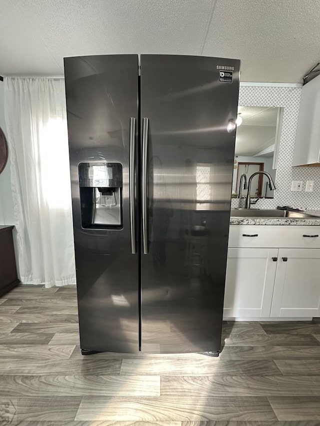 kitchen with white cabinets, black fridge with ice dispenser, and a textured ceiling