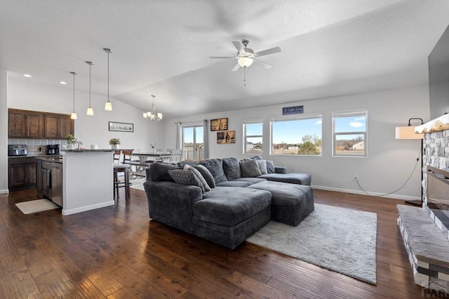living area with vaulted ceiling, ceiling fan with notable chandelier, a stone fireplace, dark wood-style flooring, and baseboards