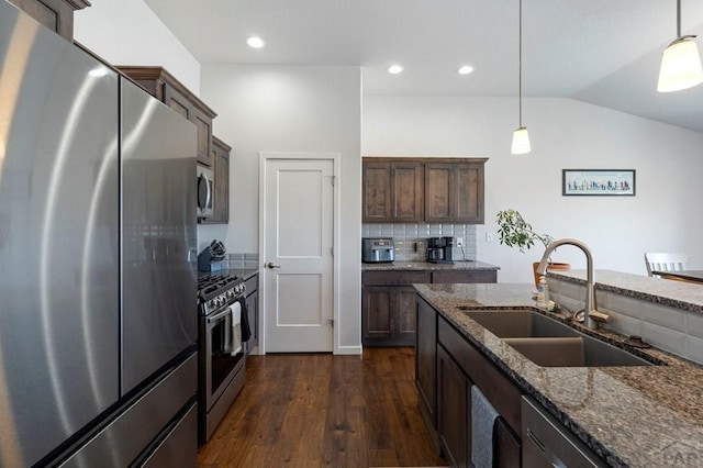 kitchen featuring dark stone countertops, appliances with stainless steel finishes, dark wood-type flooring, and a sink
