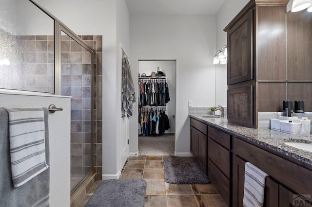 full bathroom with a sink, a shower stall, a walk in closet, double vanity, and baseboards