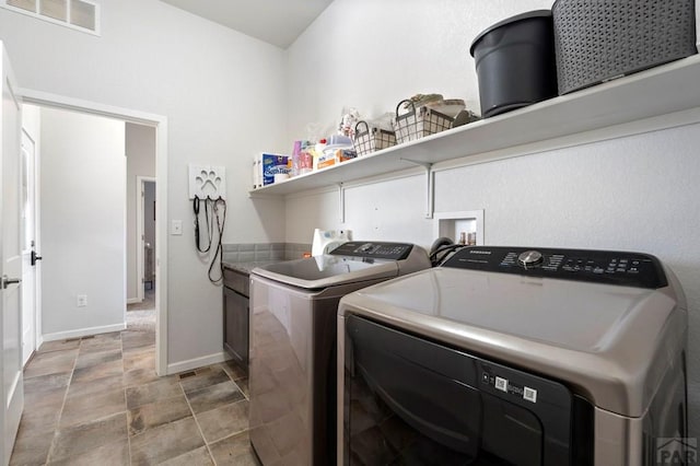 laundry room with cabinet space, washing machine and dryer, stone finish flooring, visible vents, and baseboards