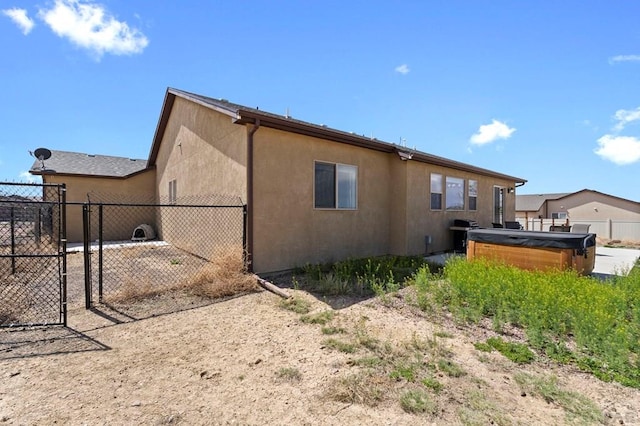 rear view of house with fence, stucco siding, a gate, and a hot tub