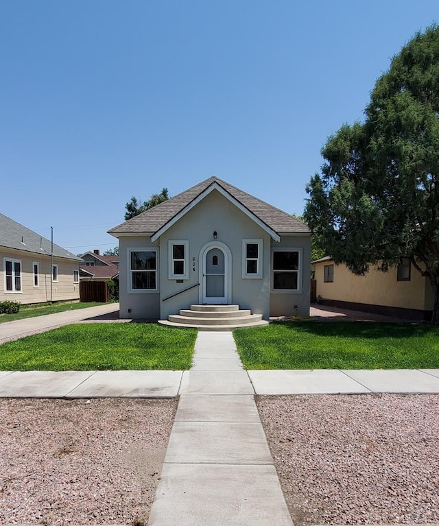 bungalow with a shingled roof, a front yard, and stucco siding