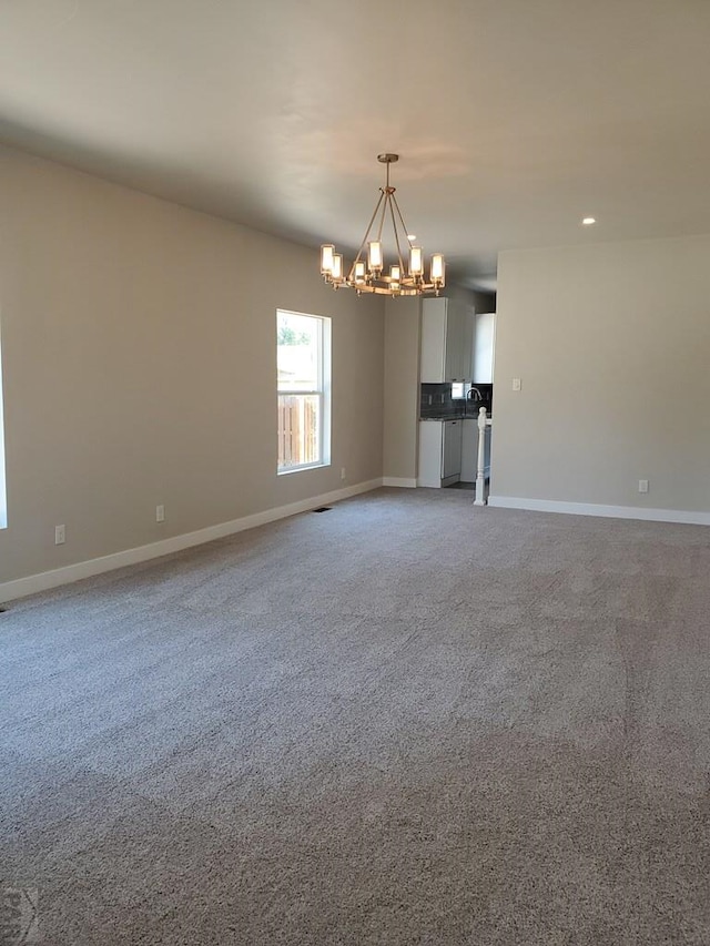 unfurnished living room featuring carpet floors, a notable chandelier, recessed lighting, visible vents, and baseboards