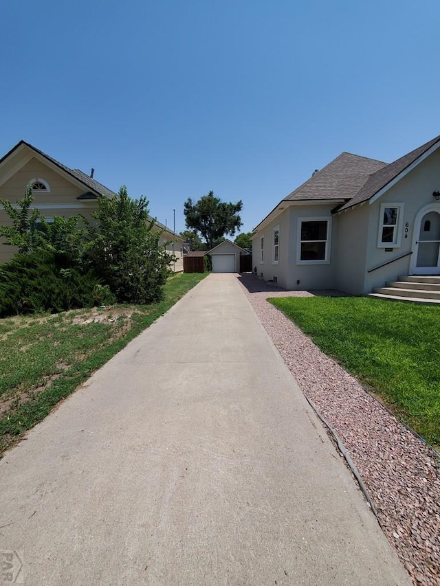 view of side of property with stucco siding, a shingled roof, a lawn, a garage, and an outdoor structure