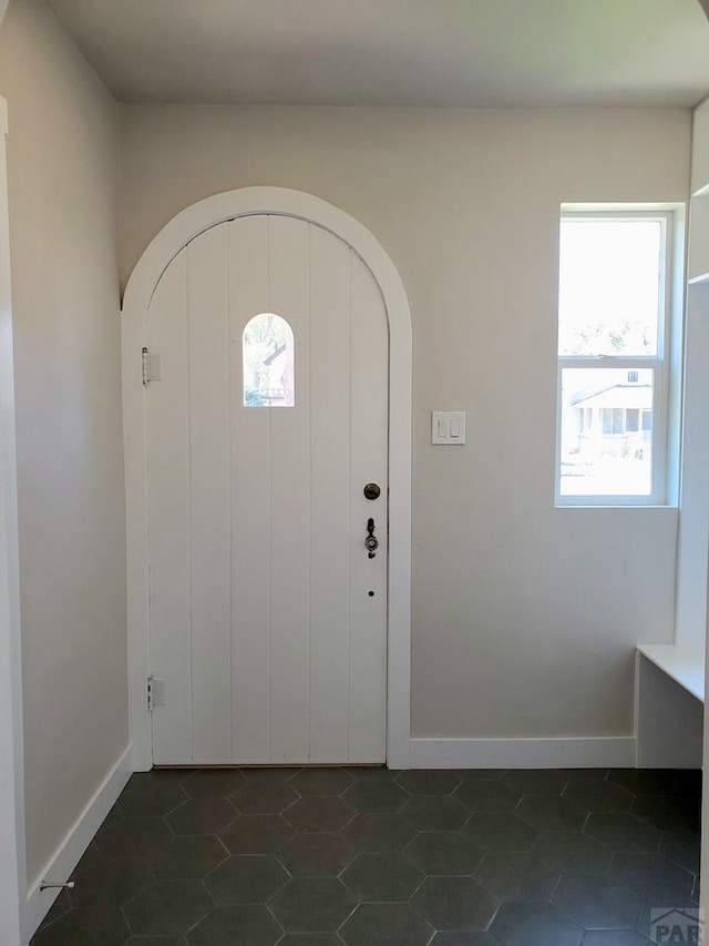 foyer entrance with dark tile patterned flooring, arched walkways, and baseboards