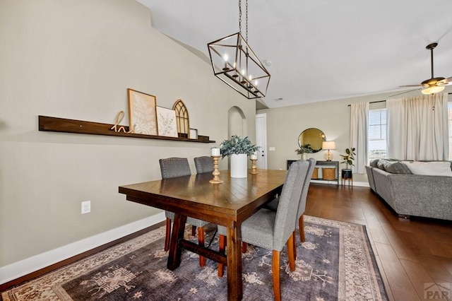 dining space with dark wood-style flooring, ceiling fan, a chandelier, baseboards, and arched walkways