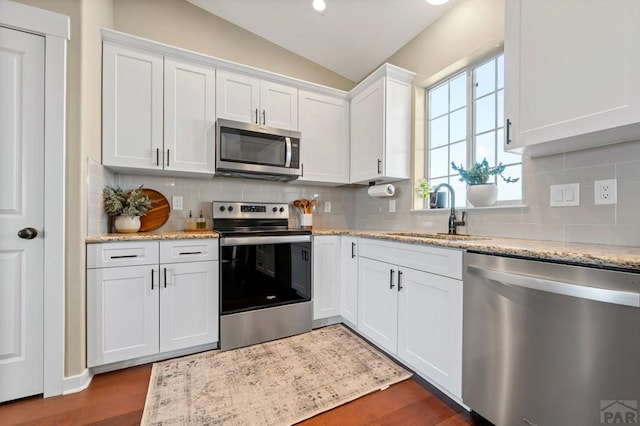 kitchen featuring appliances with stainless steel finishes, a sink, vaulted ceiling, white cabinets, and dark wood-style flooring
