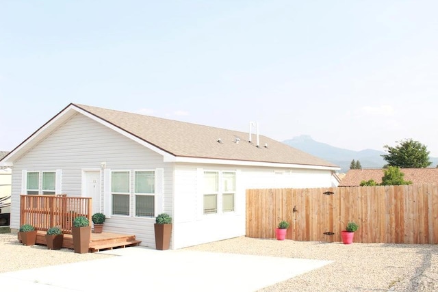 rear view of property featuring roof with shingles, fence, and a deck with mountain view