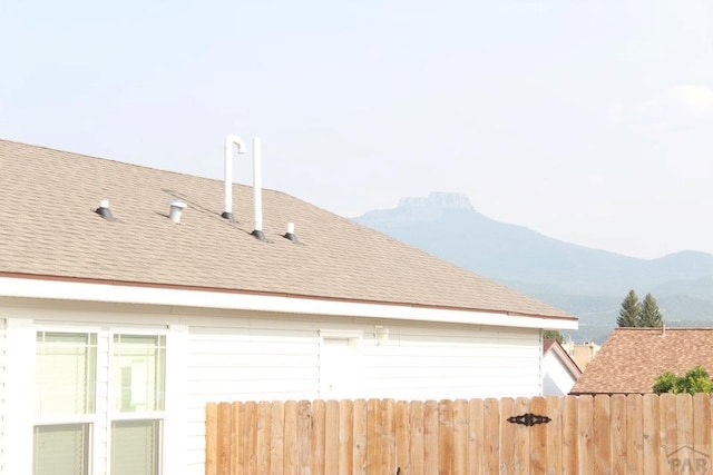 view of home's exterior featuring a shingled roof, a mountain view, and fence