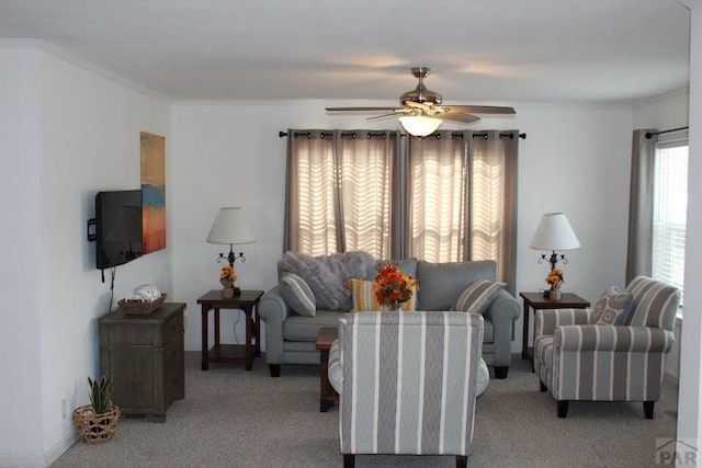 living area with ornamental molding, light carpet, and a ceiling fan