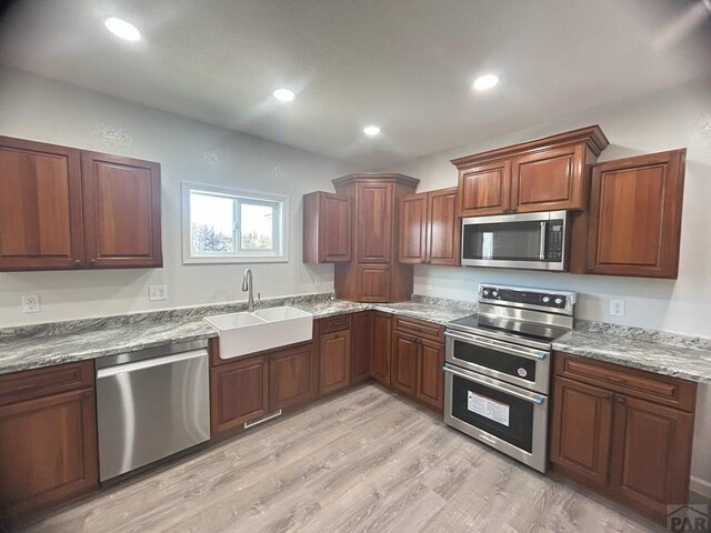 kitchen featuring recessed lighting, a sink, light wood-style floors, appliances with stainless steel finishes, and light stone countertops