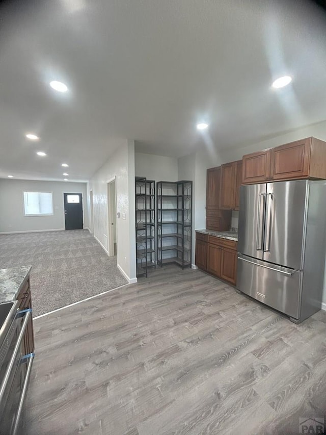 kitchen featuring high quality fridge, light stone counters, brown cabinets, open floor plan, and light wood-style floors