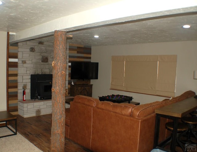 living room featuring recessed lighting, a textured ceiling, a stone fireplace, and wood finished floors