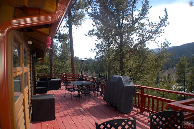 wooden terrace featuring outdoor dining area, a forest view, and grilling area