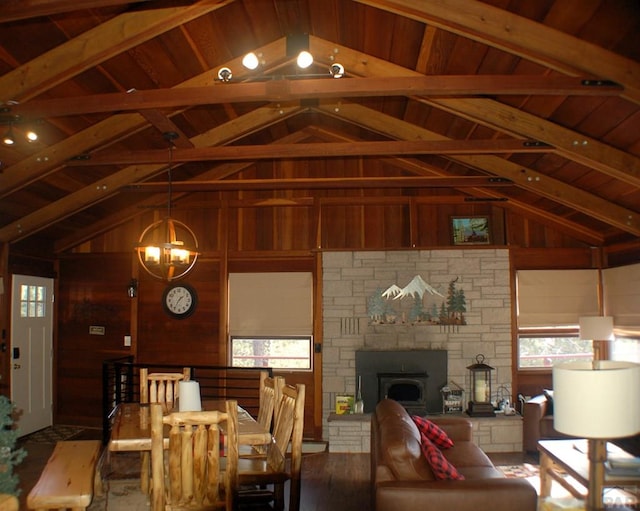 dining room featuring wooden walls, a stone fireplace, an inviting chandelier, and vaulted ceiling