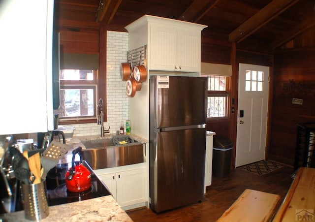 kitchen featuring beam ceiling, white cabinets, freestanding refrigerator, and a sink