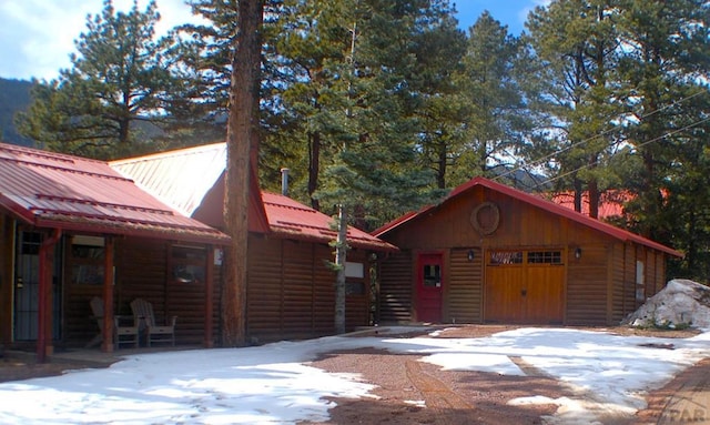 view of front of house featuring log veneer siding, metal roof, a detached garage, and an outdoor structure