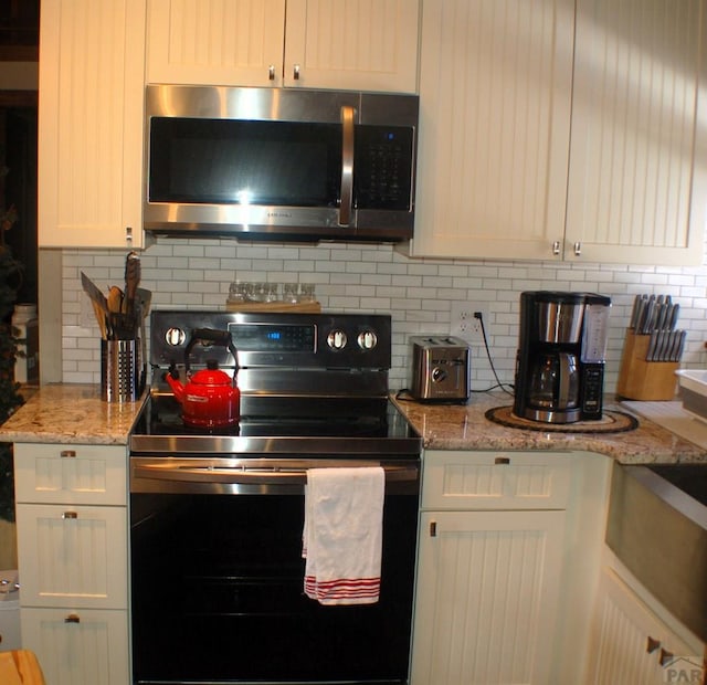 kitchen with light stone countertops, electric range oven, white cabinetry, stainless steel microwave, and tasteful backsplash