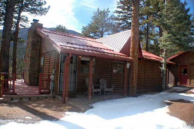 view of front of home featuring a chimney, log veneer siding, and metal roof