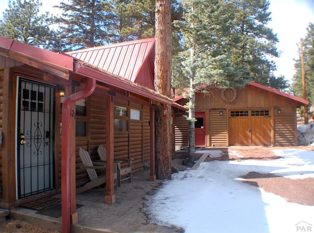 view of property exterior featuring faux log siding, driveway, metal roof, and a garage