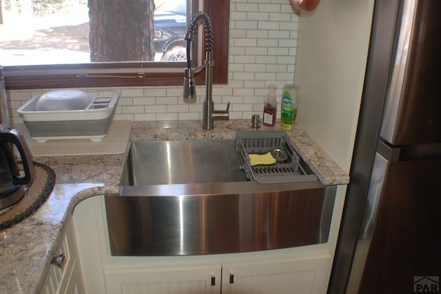 interior details with tasteful backsplash, freestanding refrigerator, light stone counters, and a sink