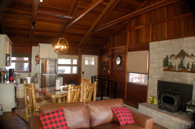 living room with vaulted ceiling with beams, wood walls, wood ceiling, a wood stove, and an inviting chandelier