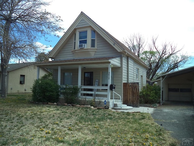 bungalow with aphalt driveway, cooling unit, covered porch, a detached garage, and a front lawn