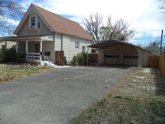 bungalow-style home featuring driveway, a porch, an outbuilding, a garage, and fence